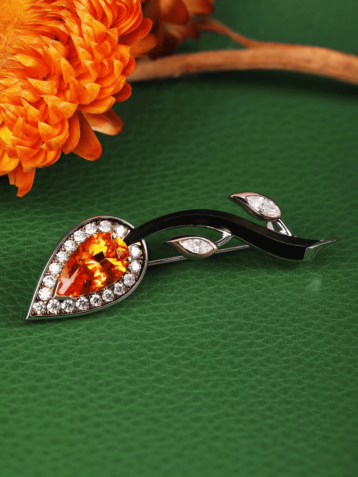 Decorative brooch with orange gemstone on a green textured surface with an orange flower.