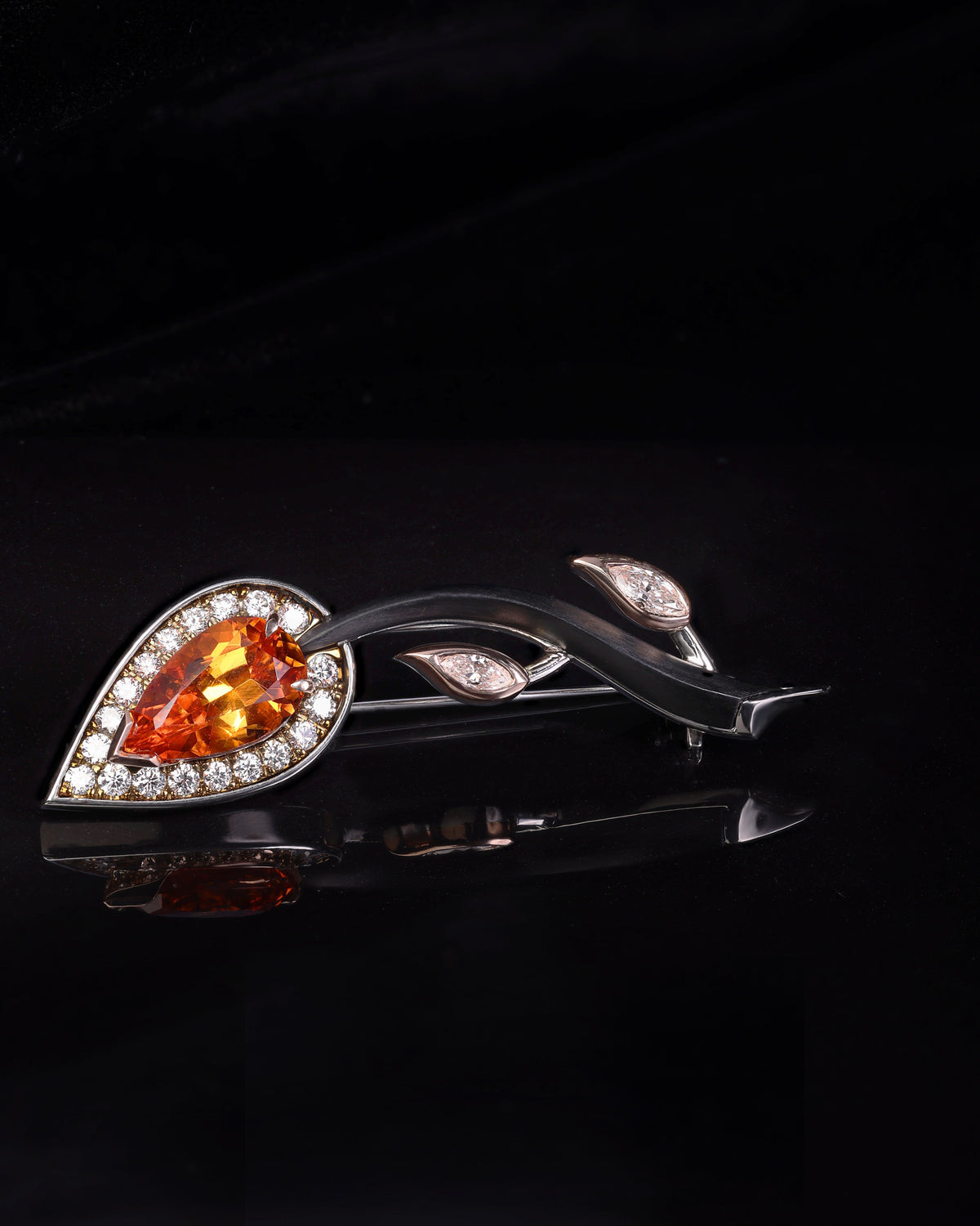 Decorative brooch with orange gemstone and silver accents on a black background