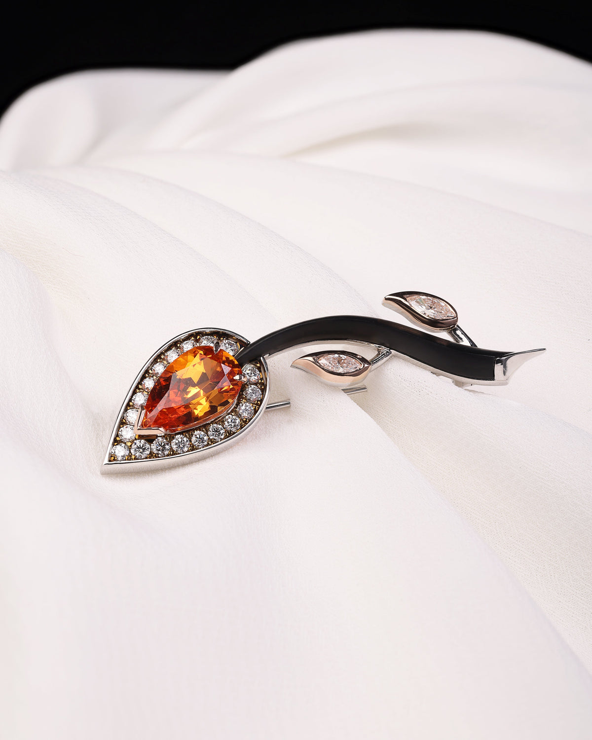 Brooch with a pear-shaped orange gemstone on a white background