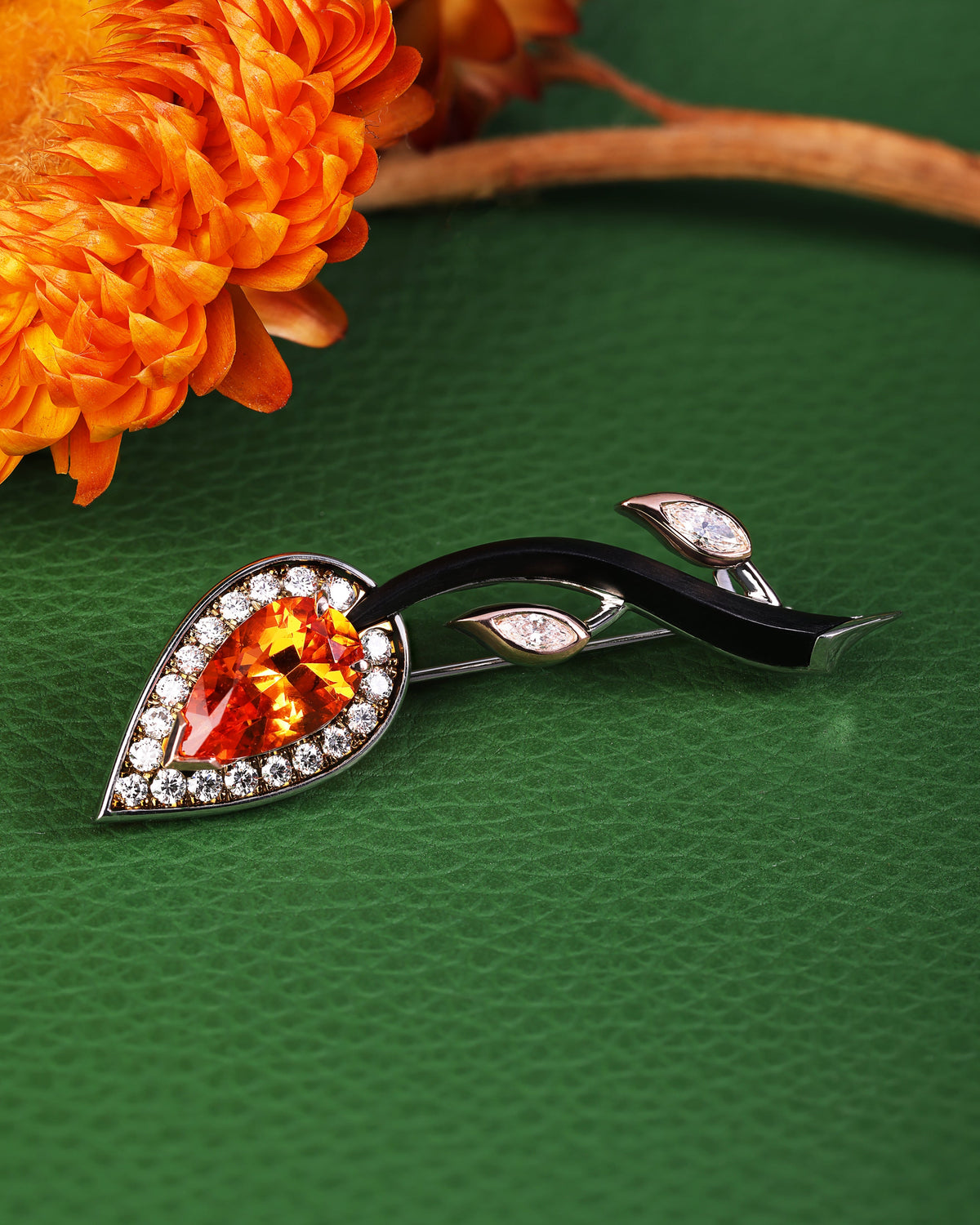 Decorative Brooch with orange gemstone on a green surface with orange flowers.