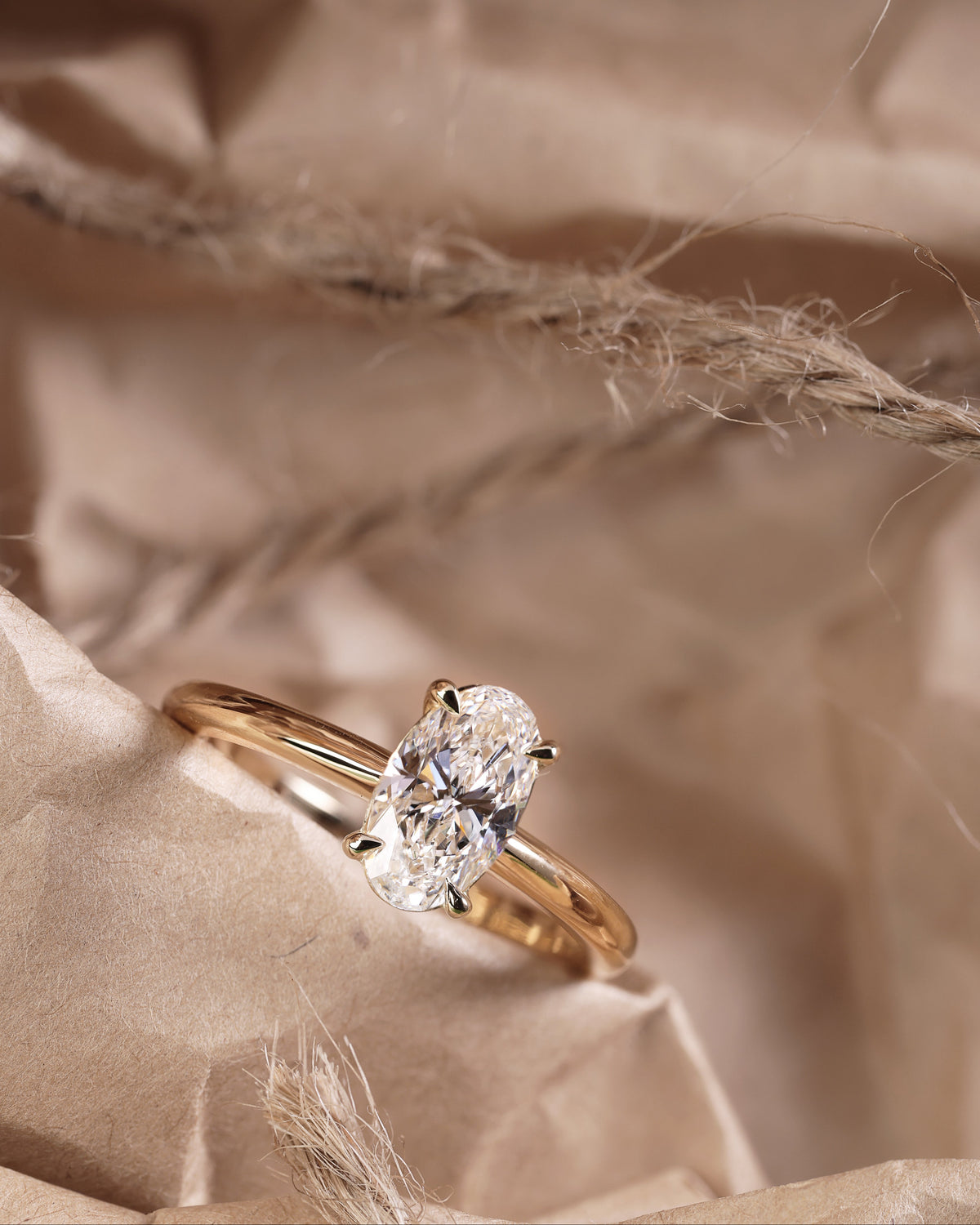 An 18ct yellow gold ring with a long oval cut natural diamond centerpiece, placed on a crumpled gold-toned paper.