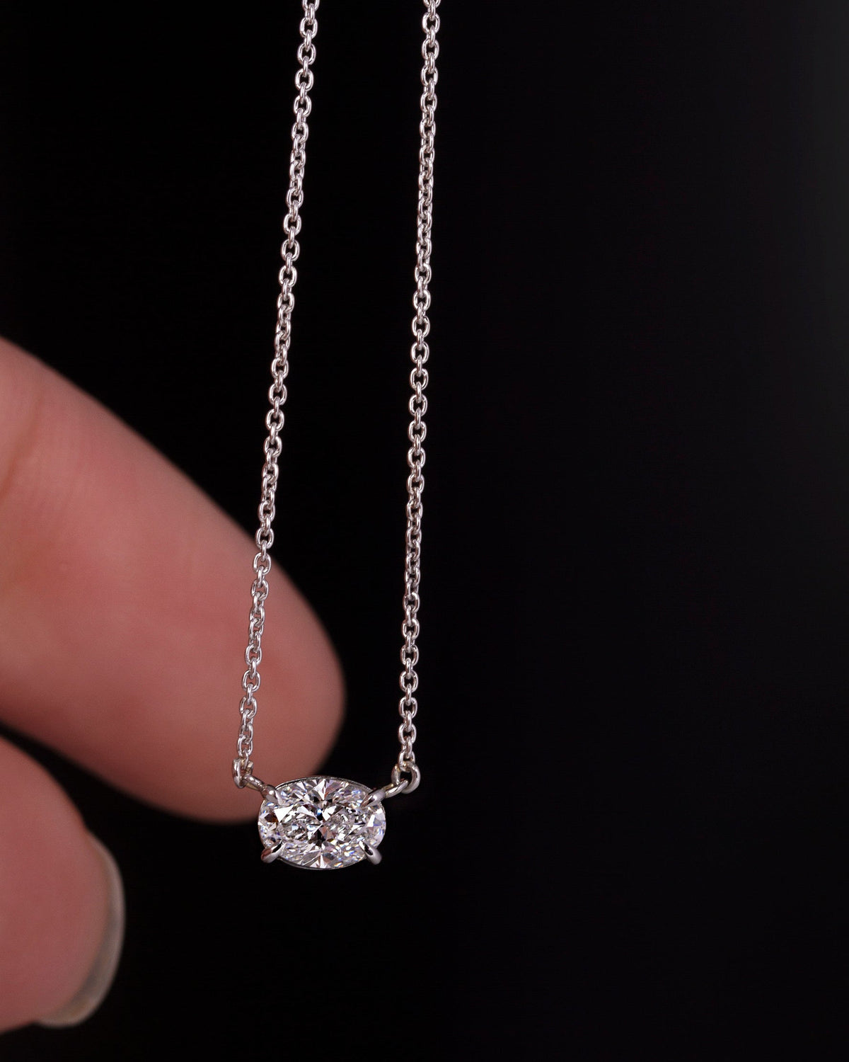 A platinum pendant featuring an oval cut diamond centerpiece, attached to a fine trace platinum chain.