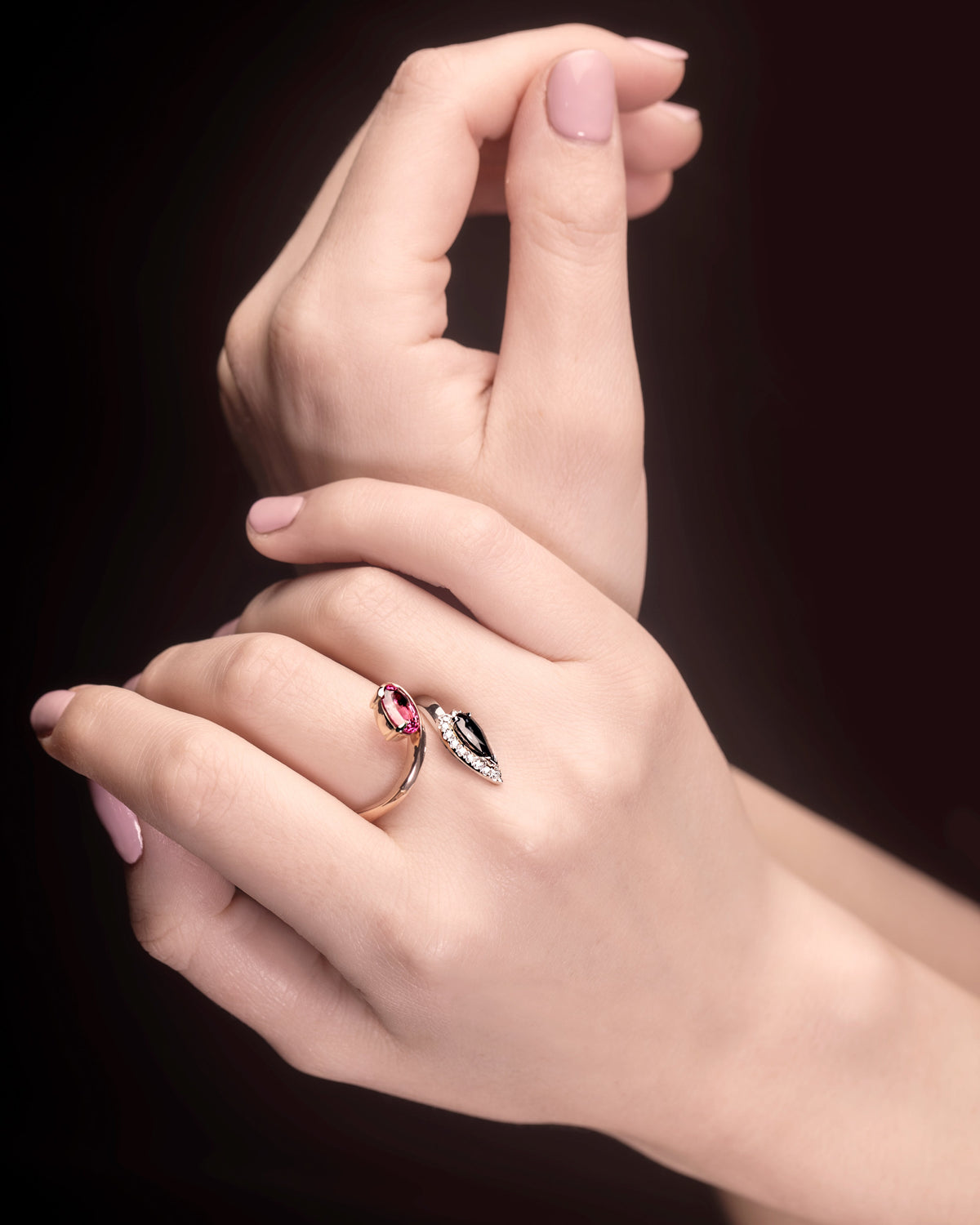 A hand displaying a ring with a pink spinel and pear cut grey spinel, surrounded by round brilliant cut diamonds set in platinum and 18ct rose gold.