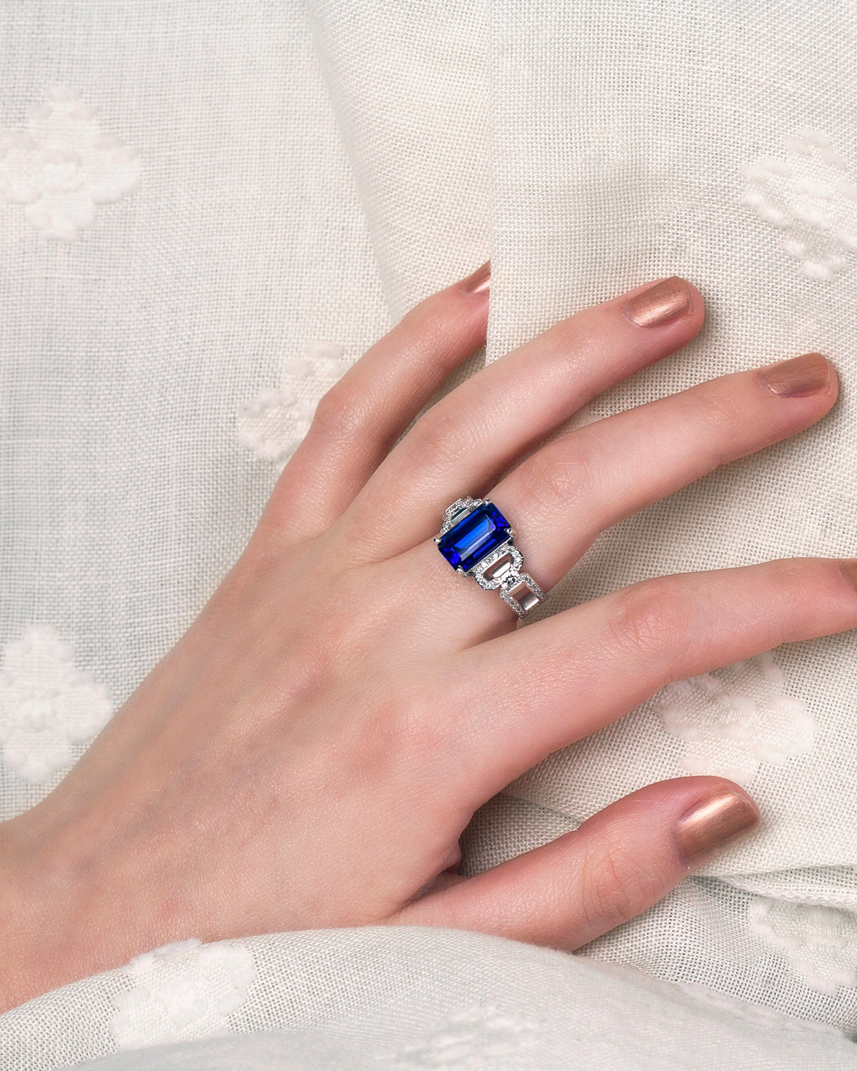 A hand wearing the bespoke link design ring with an emerald cut Tanzanite and diamonds set in 18ct white gold.