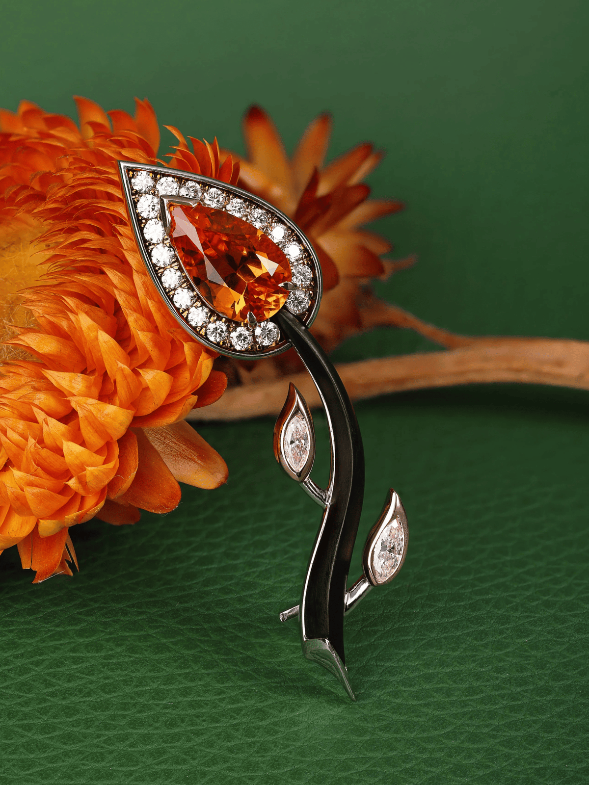 Ornate brooch with orange gemstone on an orange flower against a green background