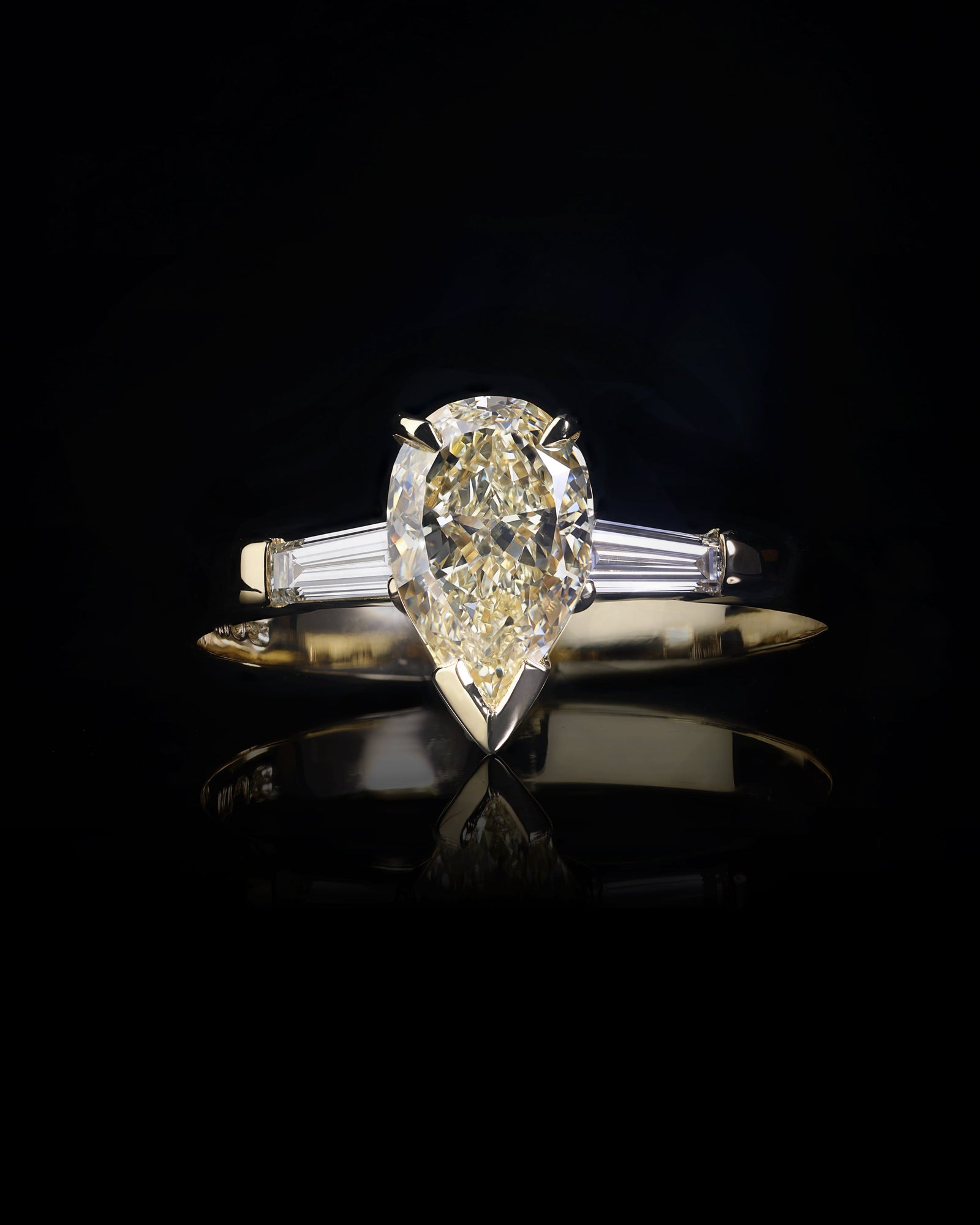 An 18ct yellow gold diamond ring featuring a pear cut fancy light yellow diamond with two tapered baguette diamonds on either side, set on a dark background.