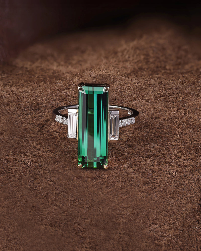 A green Tourmaline and diamond ring with a platinum band and 18ct yellow gold setting, displayed on a brown surface.
