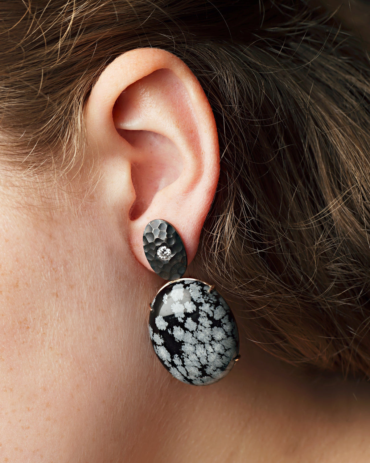 A close-up image of a person wearing 18ct Rose Gold earrings featuring round brilliant cut diamonds and cabochon cut snowflake obsidian gemstones.